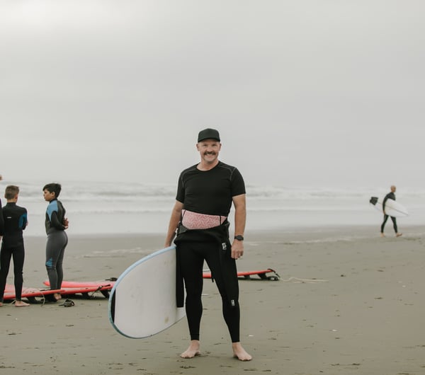 Hamish Evans at the beach smiling to camera whilst wearing a wet suit.