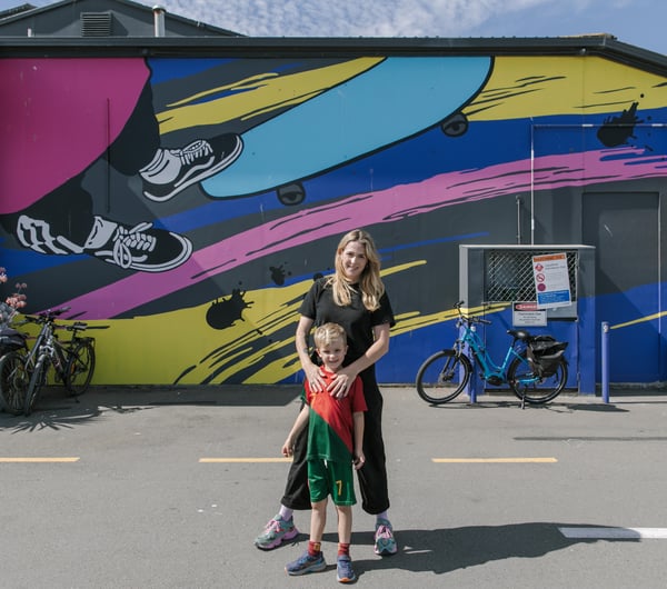 A woman and her son standing in front of a colourful mural painted on the exterior of a building.