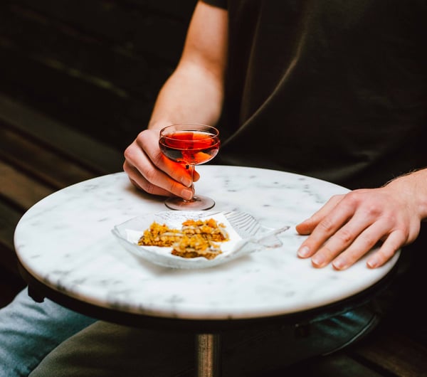 A hand holding a glass of rose next to a plate of food.