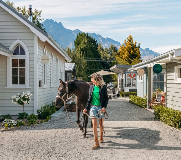 A woman and horse walking down a little country lane on a sunny day.