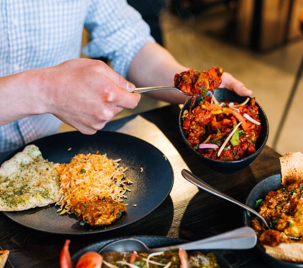 A man's hand serving himself at an Indian restaurant.