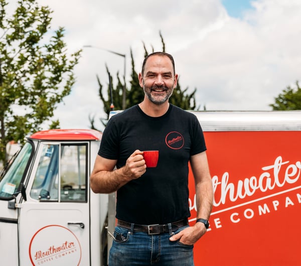 A man holding a red cup of coffee outside a coffee cart.