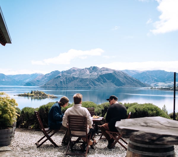 Three men are sitting at an outdoor table overlooking the lake.