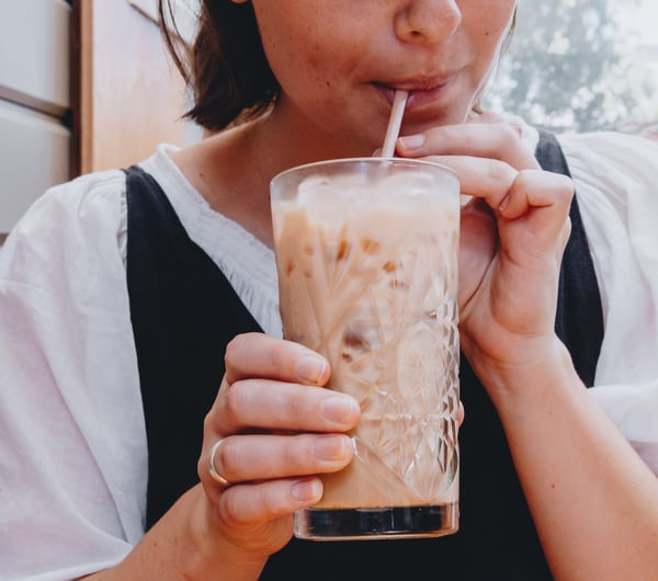Close up of a woman sipping on an iced coffee in a big glass.
