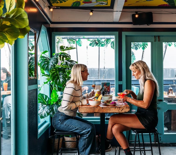 Two women dining at a high table inside a green painted room.