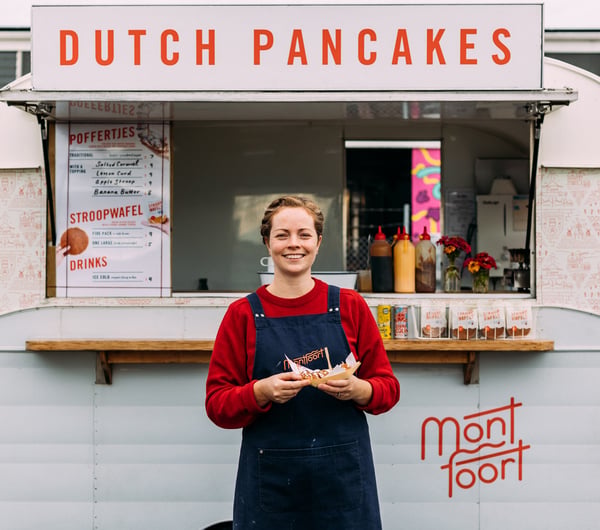 A woman holding Dutch pancakes in front of a white caravan.