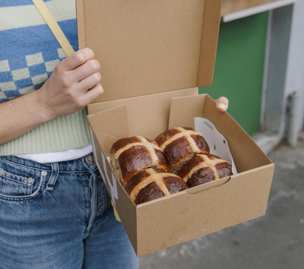 Person holding box of four Hot Cross Buns outside Grizzly in Christchurch
