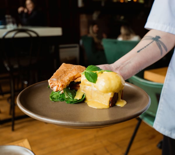 Someone holding a plate of eggs hollandaise with smoked salmon on the side