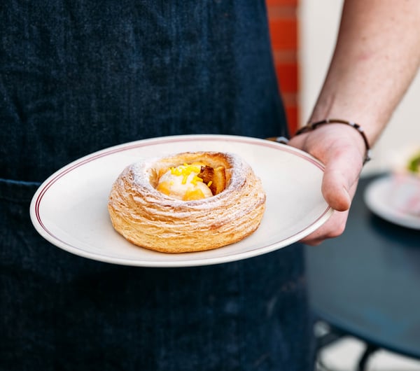 A hand holding a pastry on a plate.