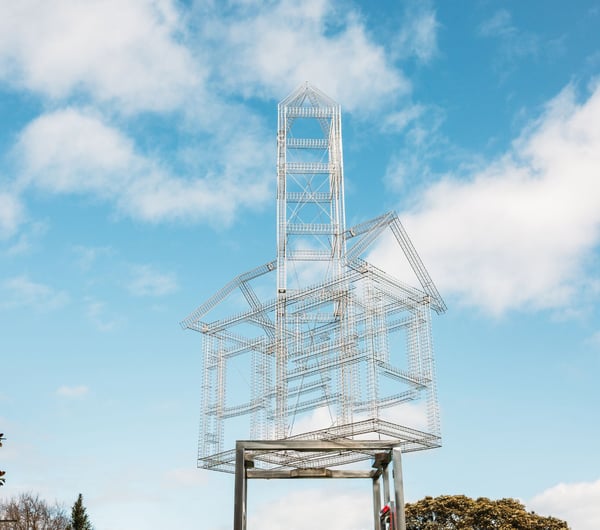 A sliver metal sculpture of a house frame on stilts.