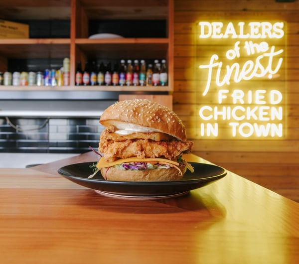 A Chicken burger on a black plate sitting on a wooden bench.