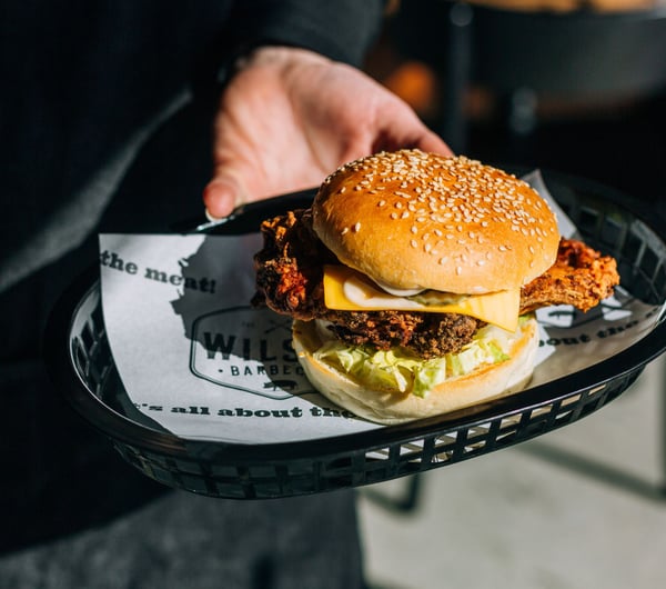 Someone holding a fried chicken burger with a sesame seed bun.