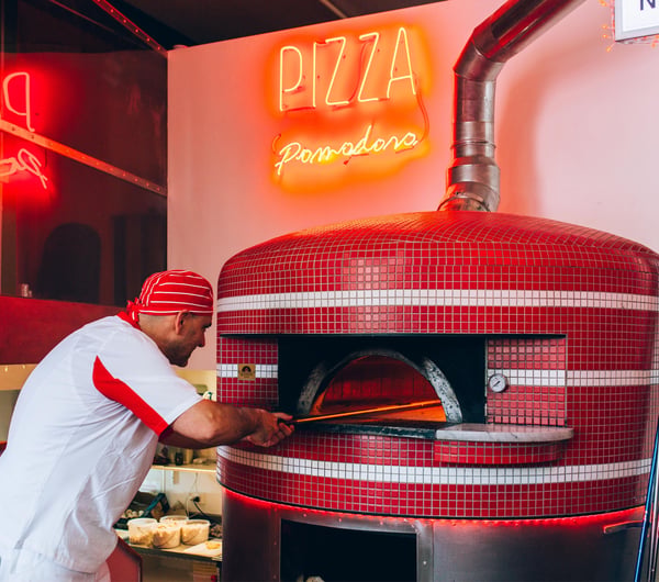 A man putting a pizza in a wood fired oven.
