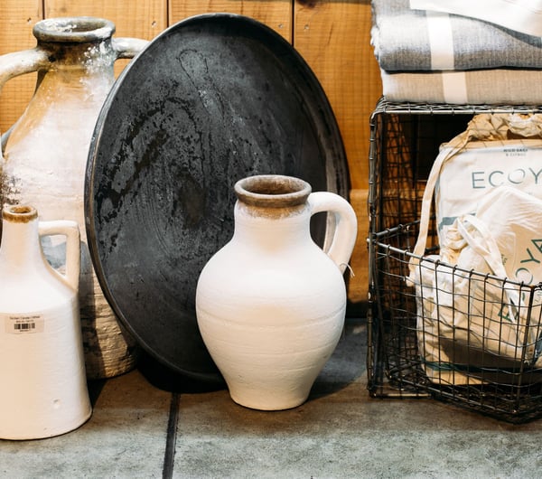 Two tall white concrete look vases on the floor next to a wire basket.