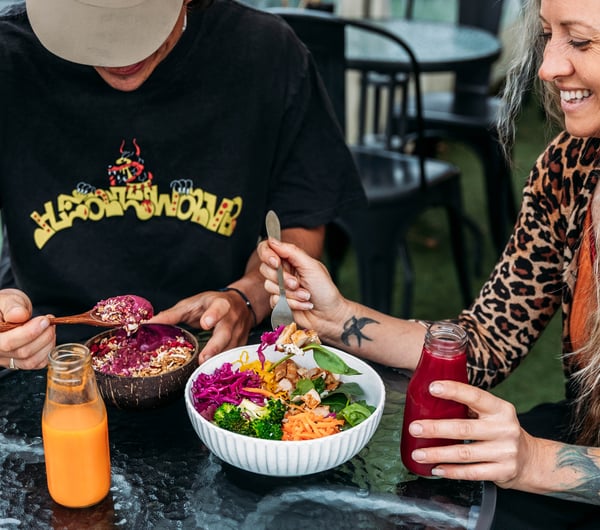 Two customers are eating buddha bowls and a glass bottle of juice is on the table.