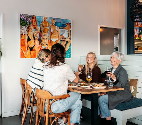 A group of women cheers their drinks over a table of food.
