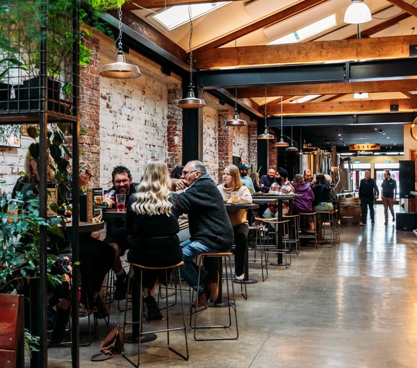 People sitting at high tops in a brick brewery building.