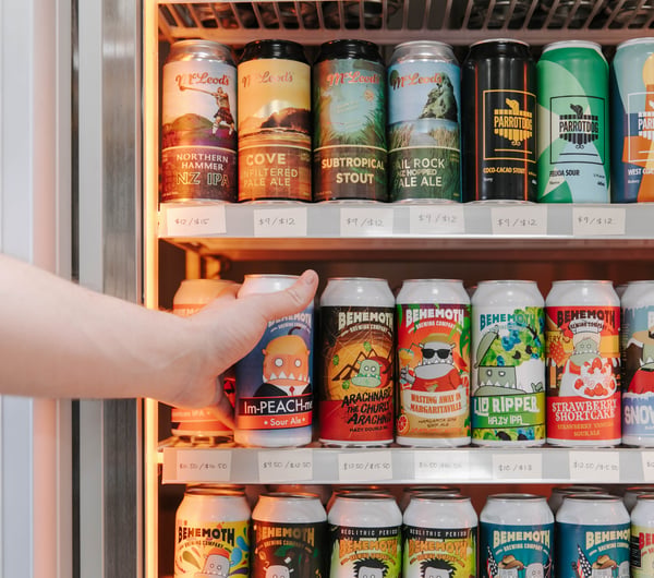 Hand reaching into fridge to grab a can of craft beer.