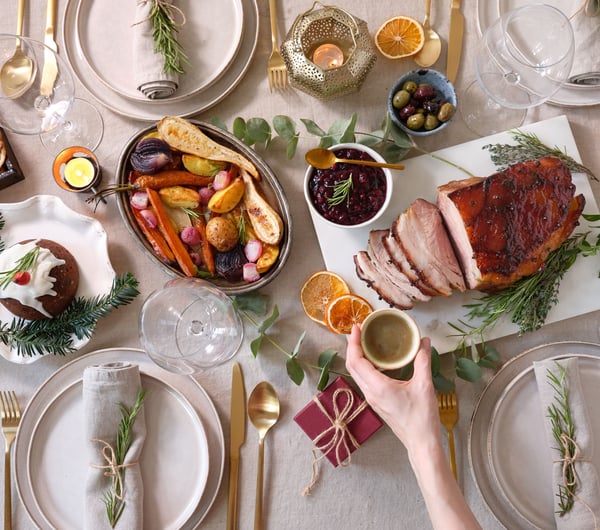 A hand holding a glass of champagne over a Christmas table setting.