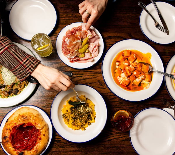 Flat lay of table full of Italian dishes at Bar Franco with people digging in with their forks