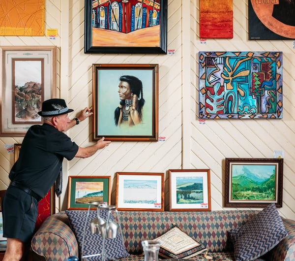 A man hanging art work on a wall inside a gallery.