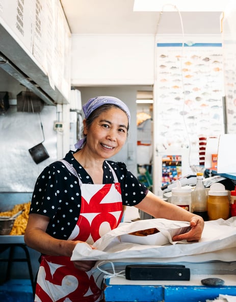 A woman packing fish and chips in a fish and chip shop.