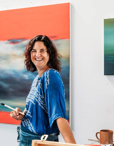 A woman holding a paint brush and smiling to camera.