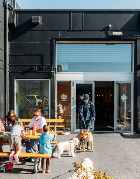 People and dogs hanging out outside a pub on a sunny day.
