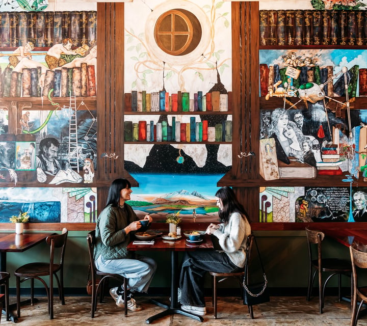Two diners sitting at a table eating with lots of decorative artwork behind them.