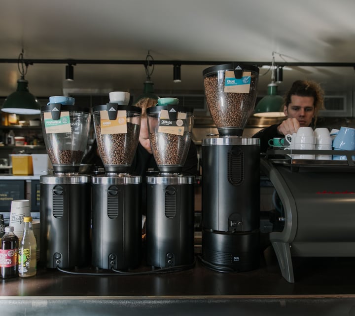 Two baristas working behind the coffee machine and four coffee bean grinders housing four different types of beans.