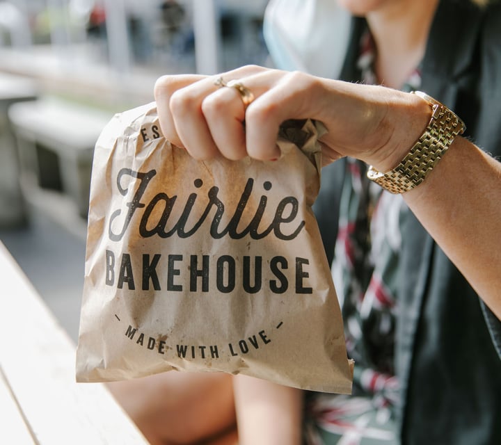 Close up of a woman holding a paper bag with 'Fairlie Bakehouse' written on it.