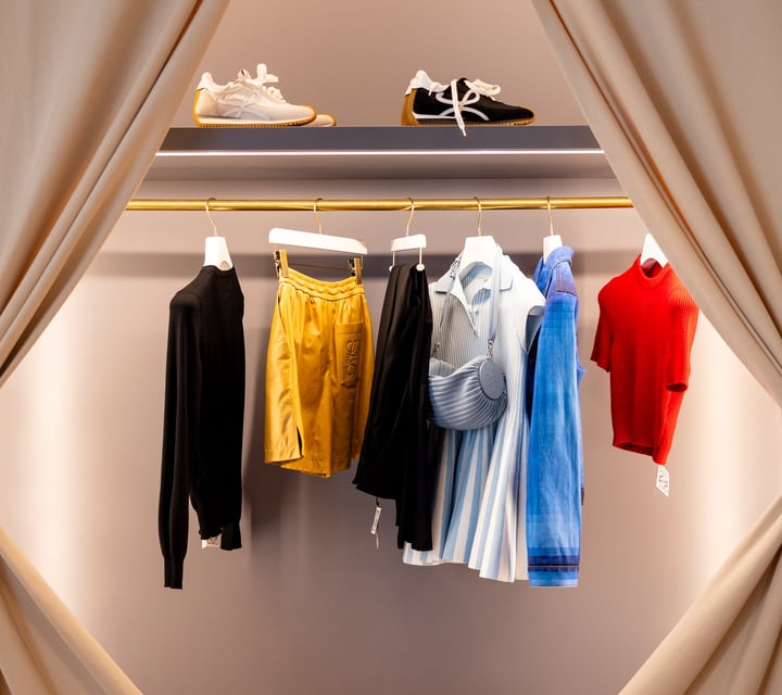 Clothes hanging on a rack framed by draped cream curtains