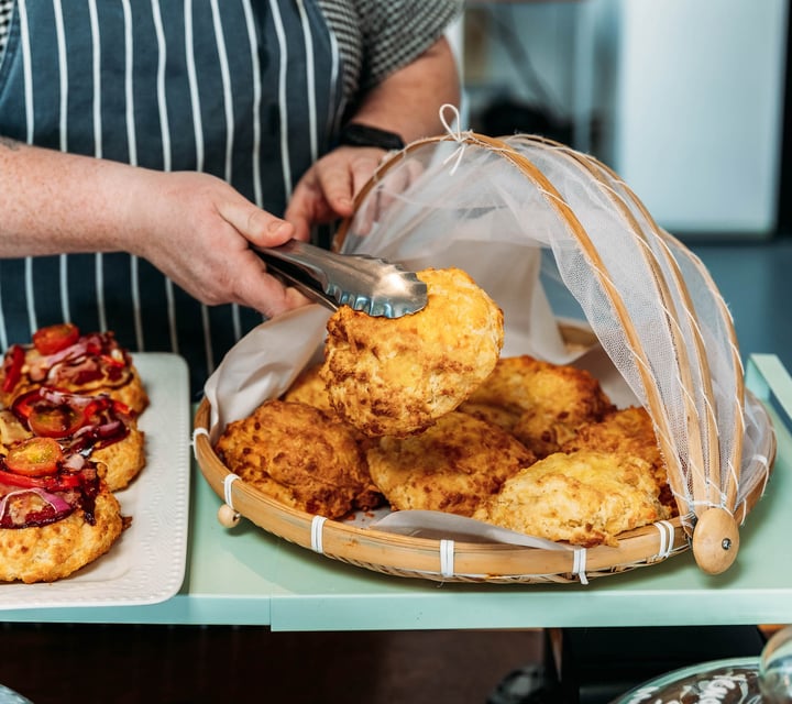 Waiter picking up a cheese scone from under mesh cloche with tongs