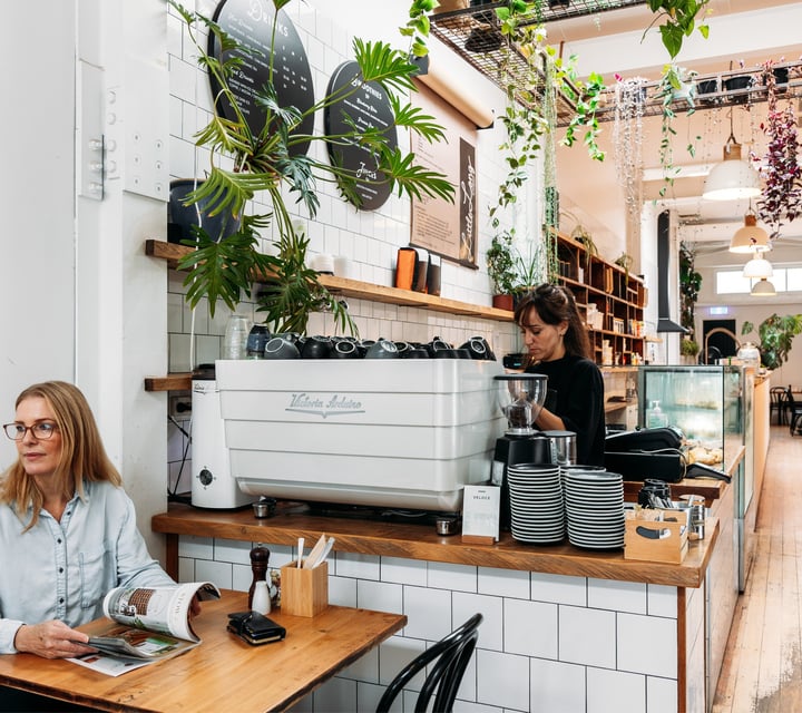 A female customer sitting next to a barista making coffee.