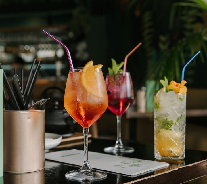 Three different cocktails on a black table with straws.