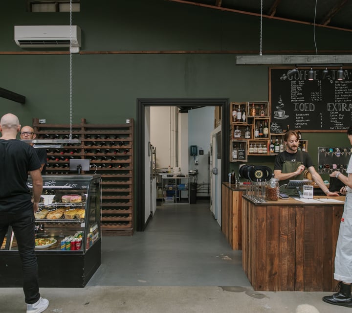 Customers standing around at a counter inside a green decorated cafe.