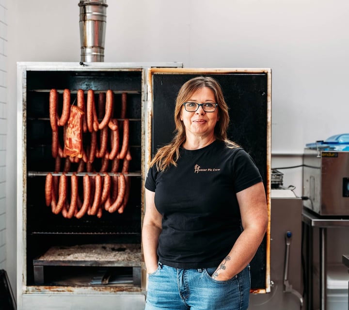 Portrait of Anna next to hanging sausages at The Polish Sausage Company in Lyall Bay Wellington