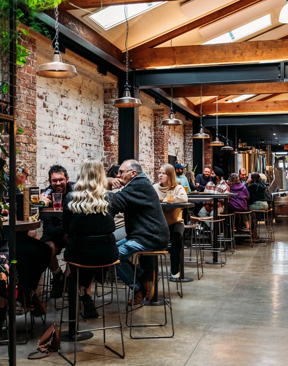 People sitting at high tops in a brick brewery building.