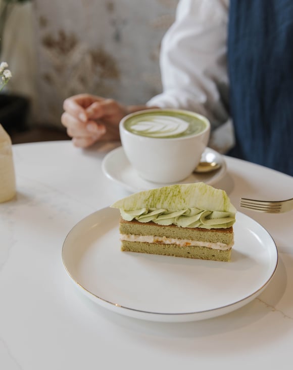 Person sitting at table at Sweet Soul Patisserie with a cup of matcha latte and a beautiful matcha flavoured patisserie