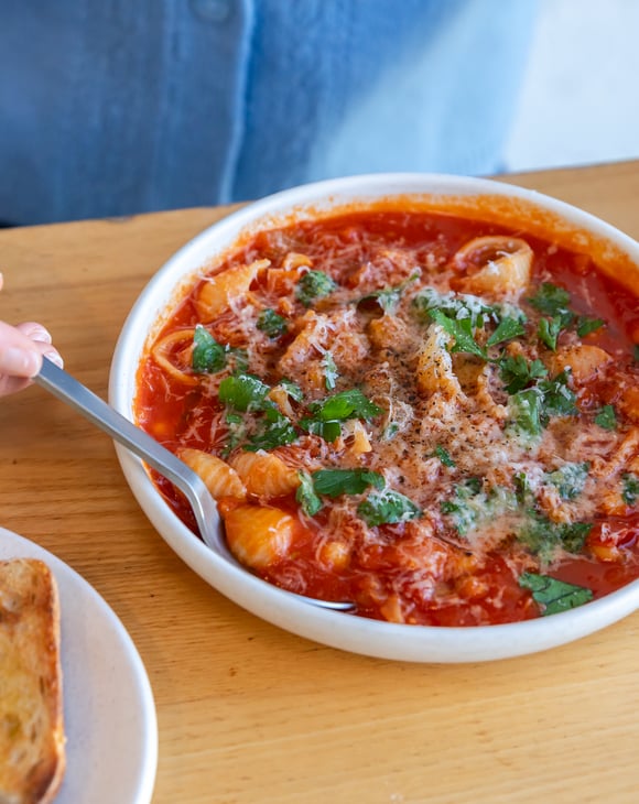 Close up of someone dipping spoon into minestrone soup from Estelle next to plate of toast