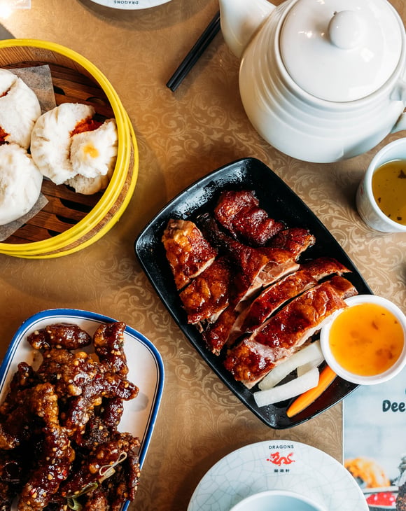 Table full of plates of Asian dishes and chopsticks.