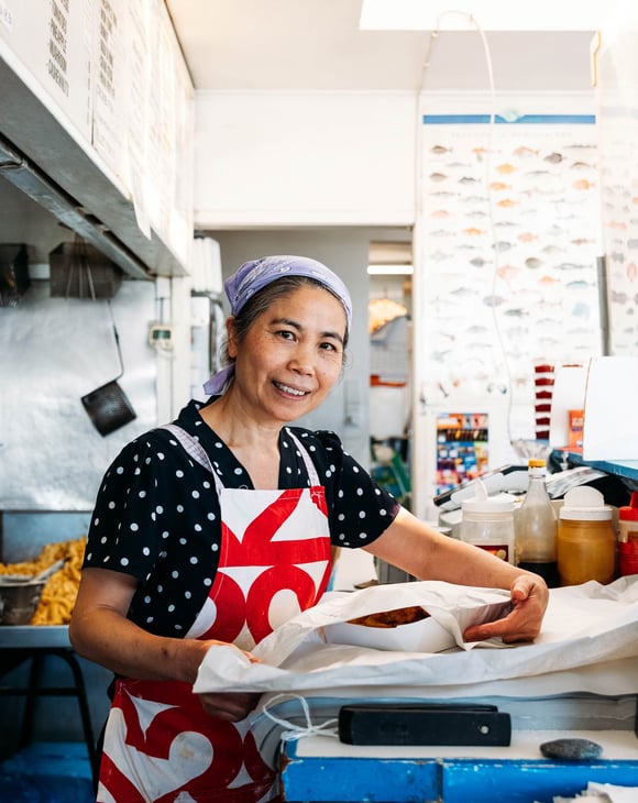 A woman packing fish and chips in a fish and chip shop.