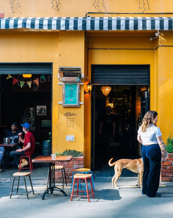 People dining outside a bar that has a yellow painted exterior.