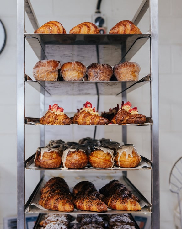 Silver trays of croissants and pastries stacked on top of each other in bakery kitchen