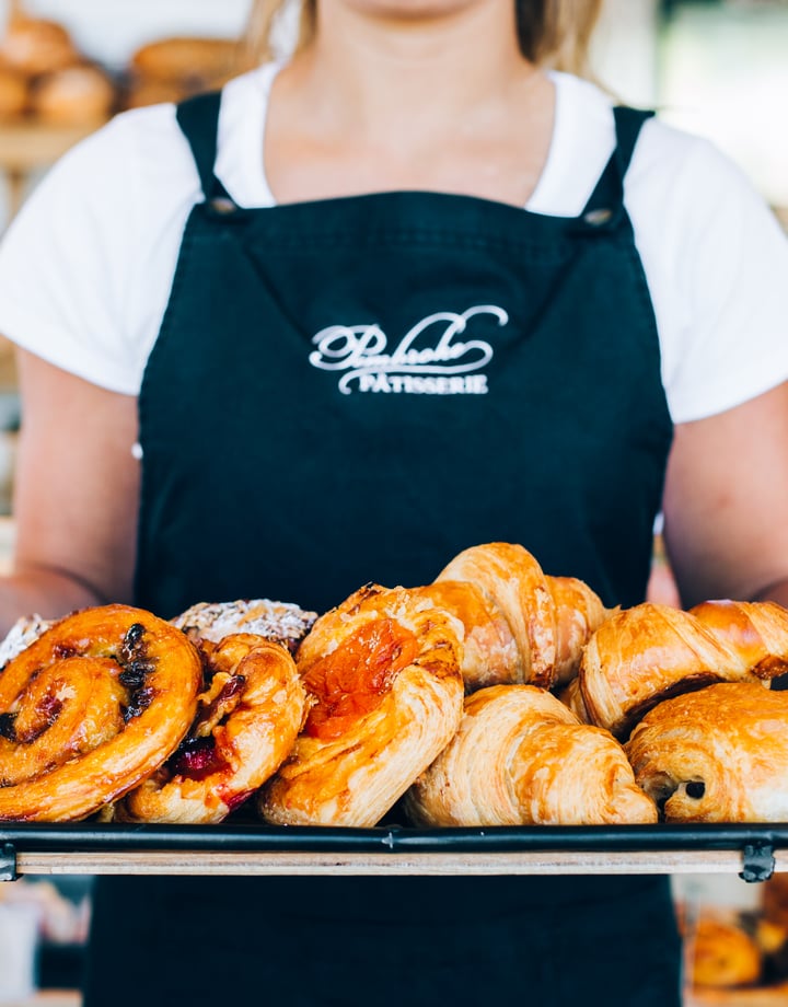 A staff member holding tray of freshly baked pastries.