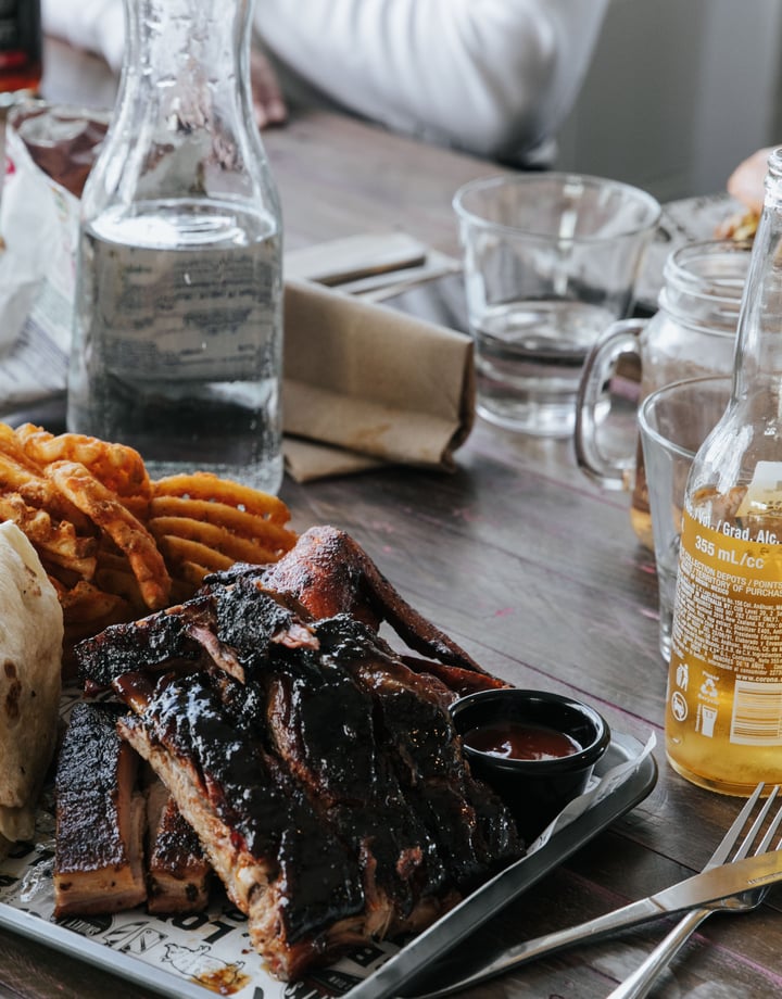 A plate of meat and chips on a table sittling alongside beers.