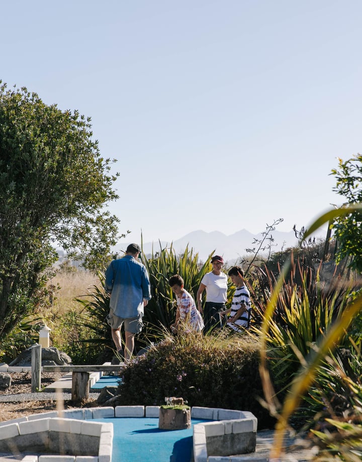 Kids playing mini golf with their parents on a sunny day.