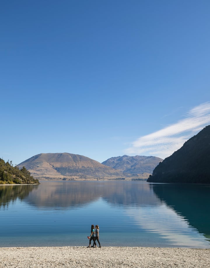 Two people walking along a lake on a sunny day.