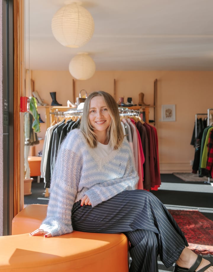 Photo of Rosie Carroll sitting on orange semi-circle couch at her secondshop Nifty in Christchurch
