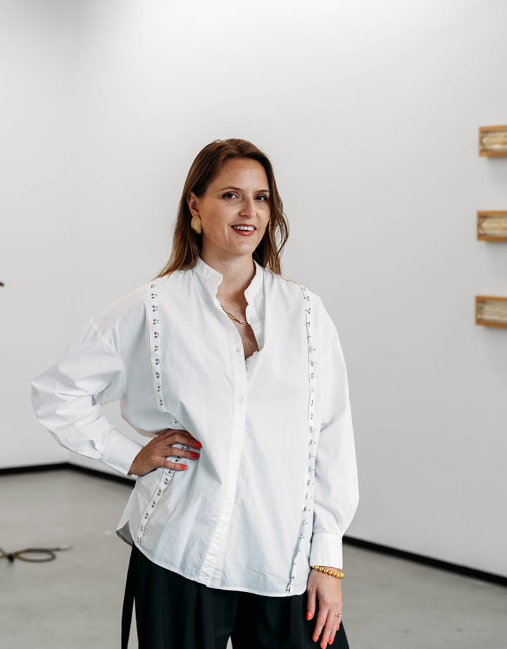 A woman with her hand on her hip in front of a gallery space.